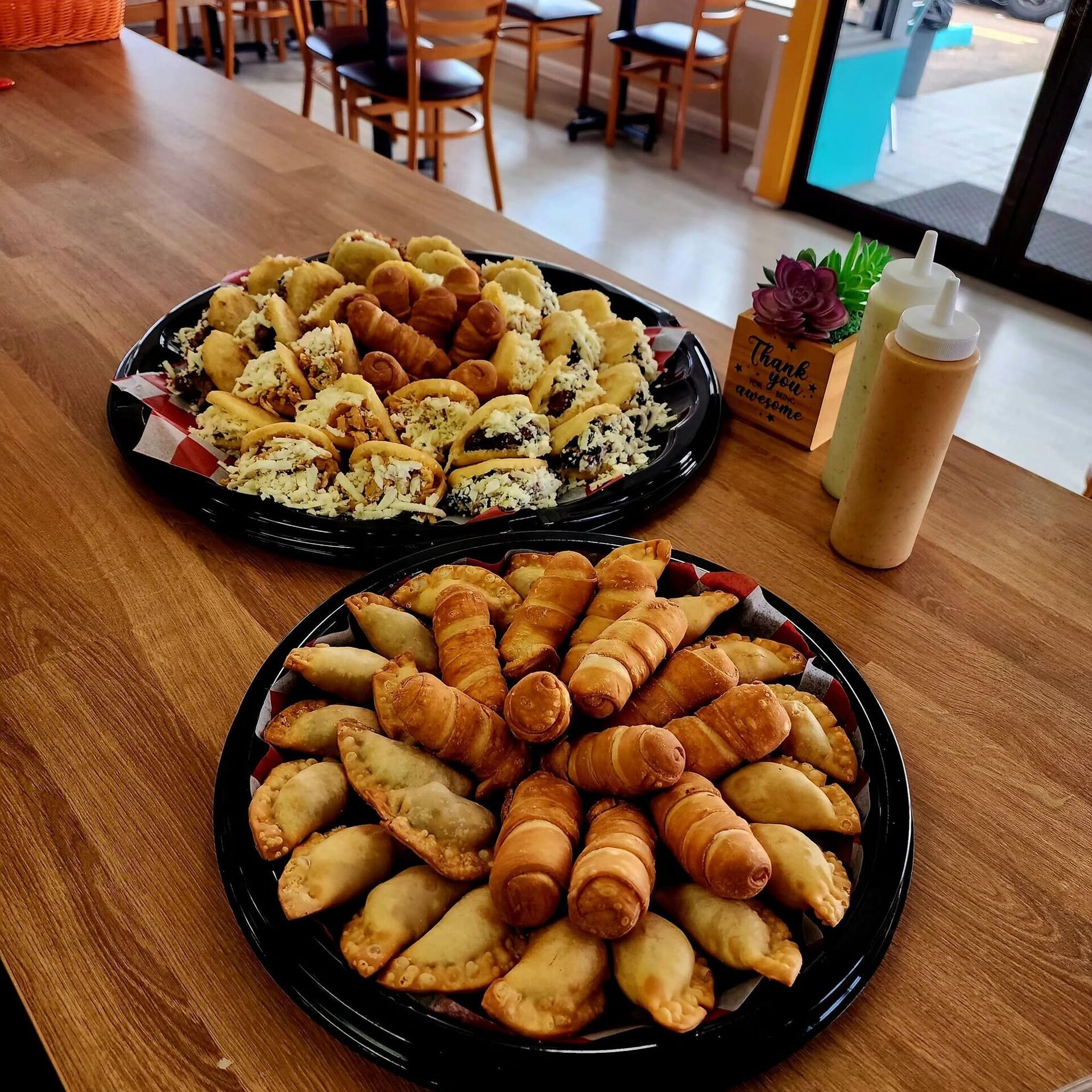 Two 1Chick 1Bro party platters of empanadas, tequeños and mini arepas set on the café's wood table