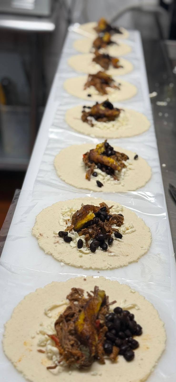Arepa and empanada rounds lined up on the prep counter in the 1Chick 1Bro kitchen, fillings laid on