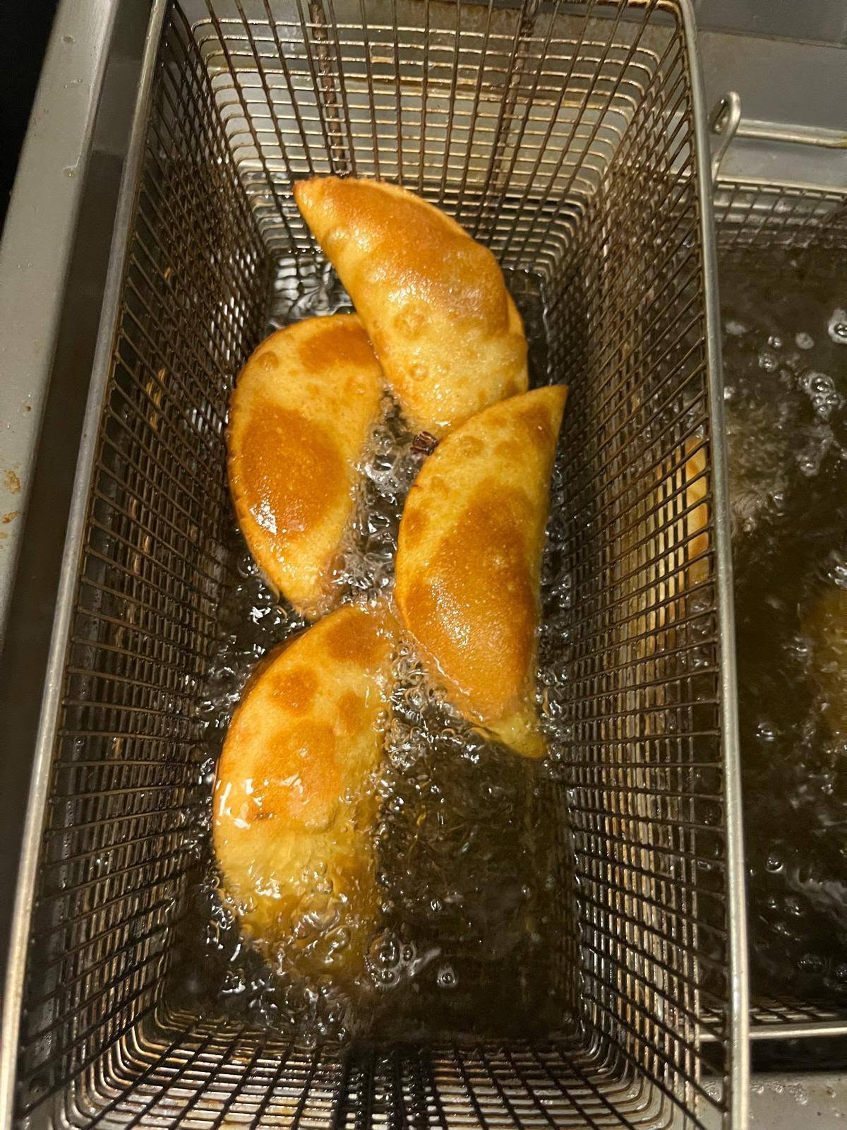 Empanadas lifting out of the fryer basket in the 1Chick 1Bro kitchen