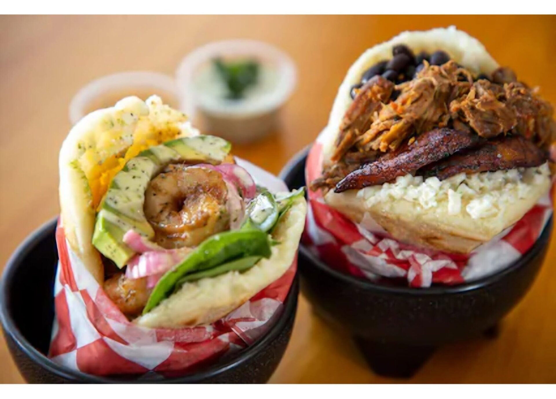 Two arepas from 1Chick 1Bro in red-check paper boats; the Pabellón on the right with shredded beef, black beans, plantain and cheese
