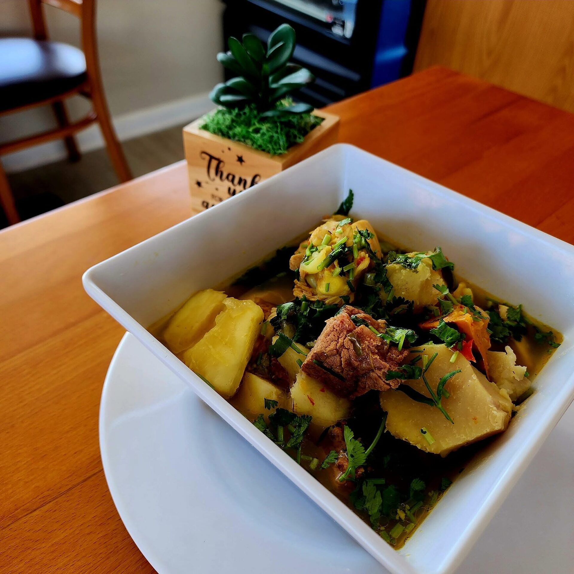 Venezuelan beef soup with potato and greens in a square bowl