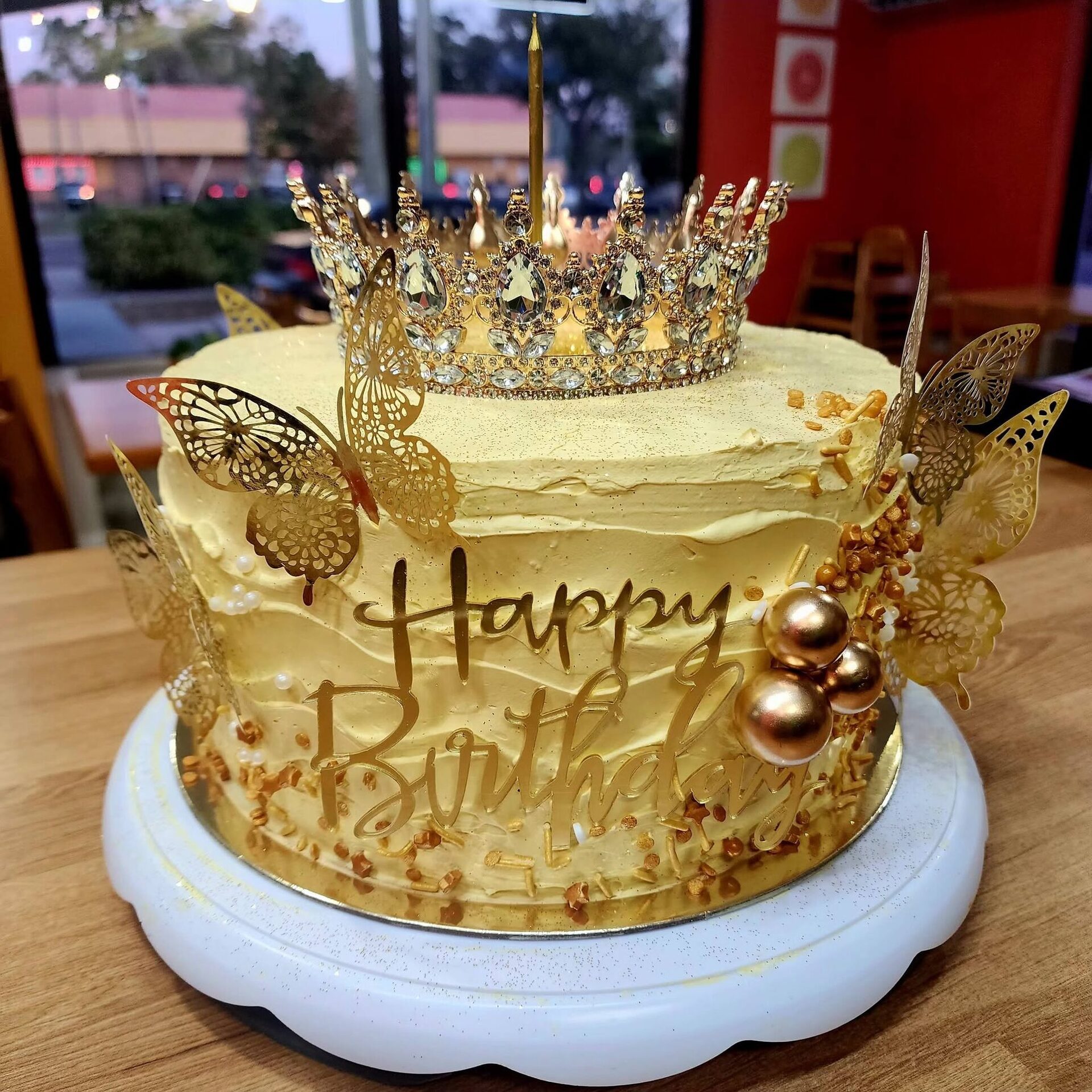 A 1Chick 1Bro gold crown birthday cake with butterflies by the front window at dusk