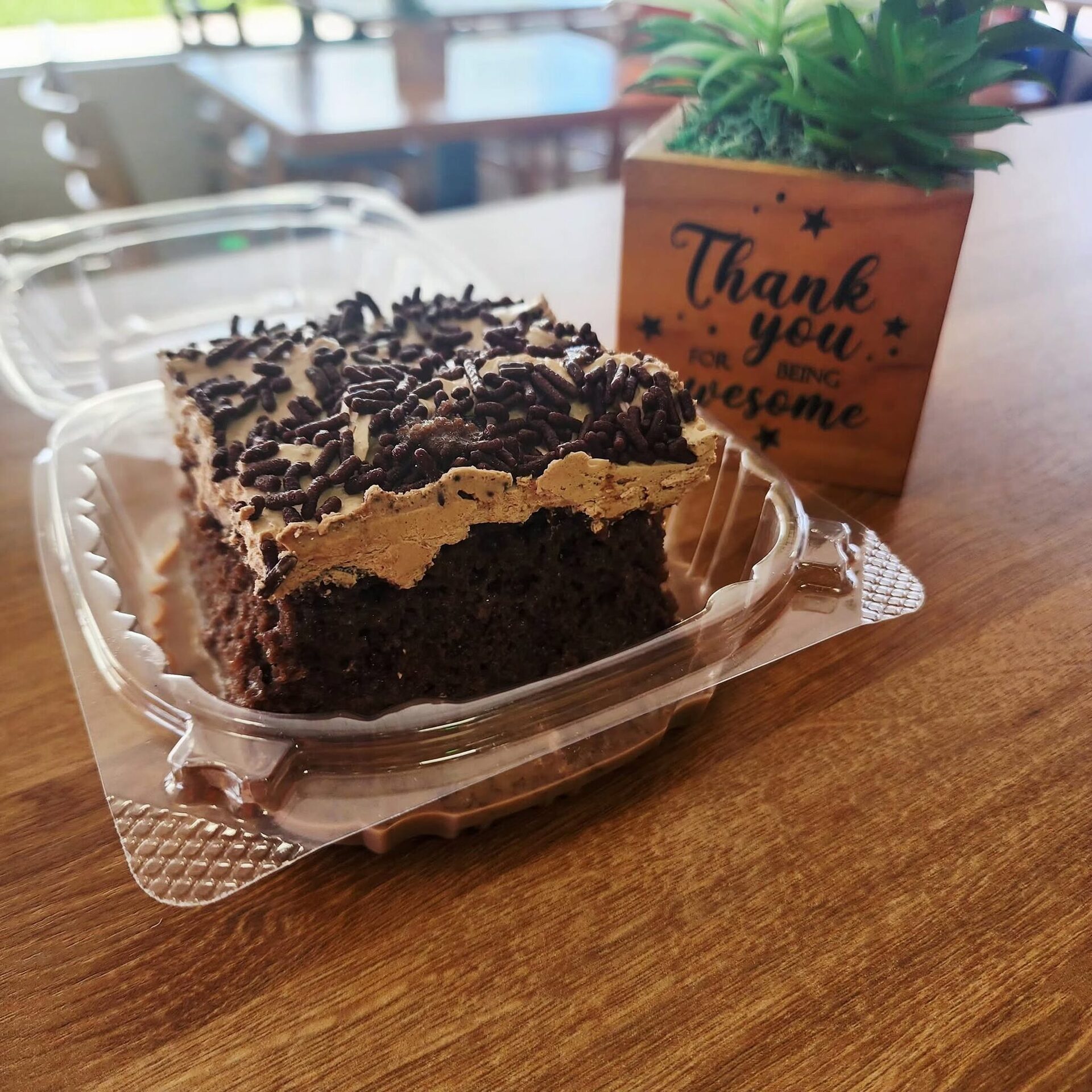 A slice of chocolate cake with cookie crumble in a to-go clamshell