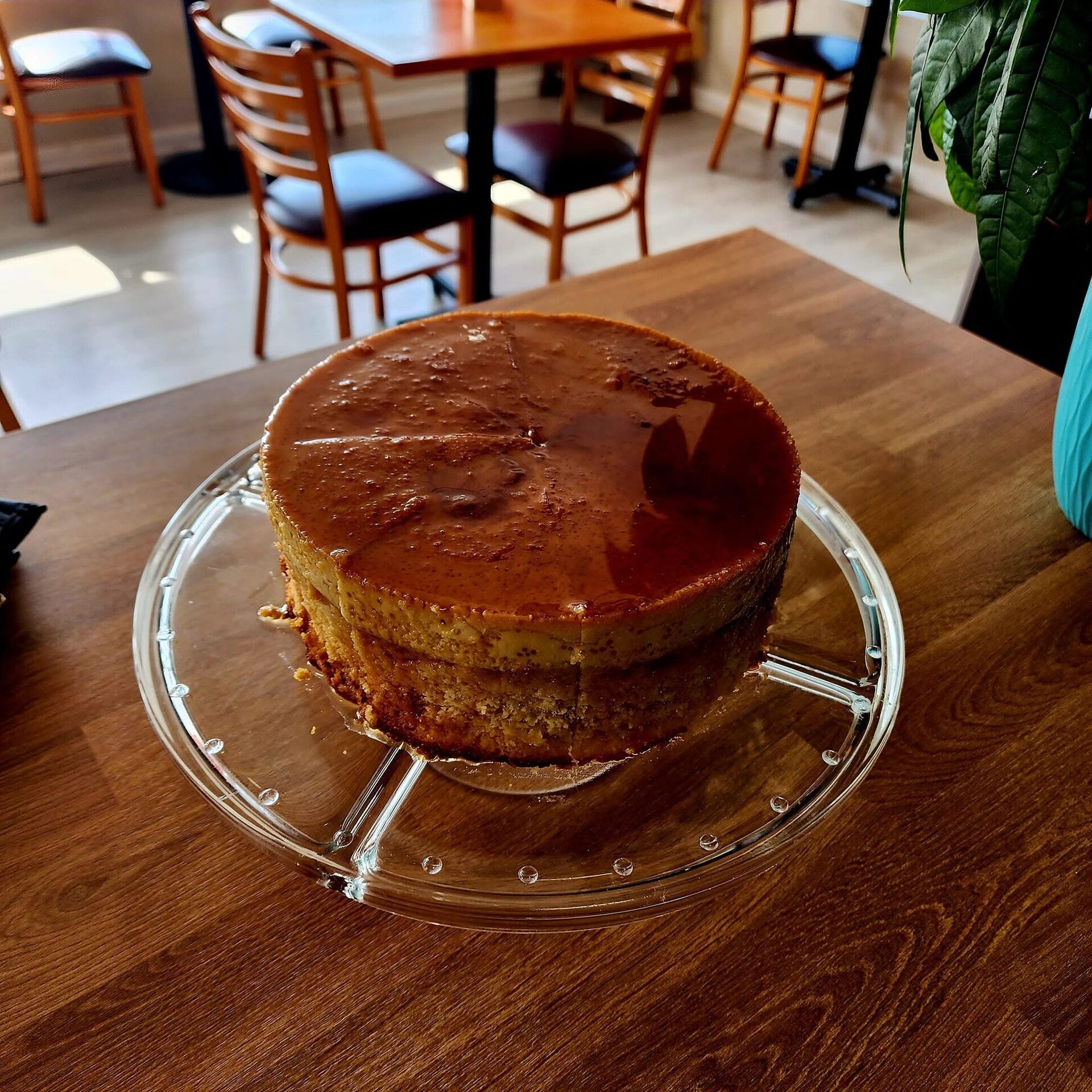 Caramel quesillo cake on a glass stand in the orange-walled dining room