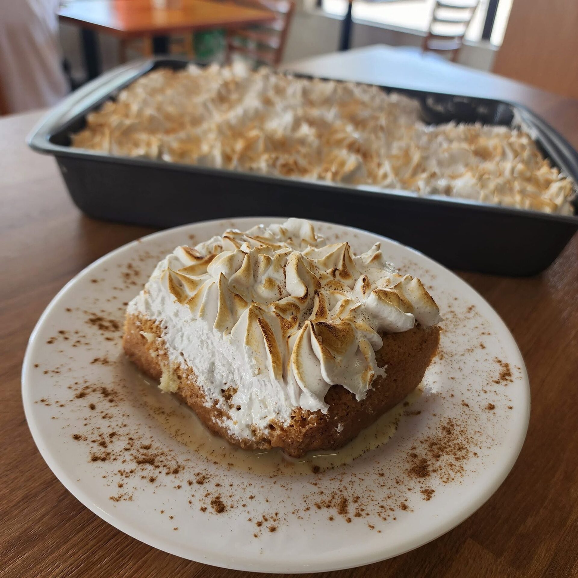 A slice of tres leches with torched meringue beside the full pan
