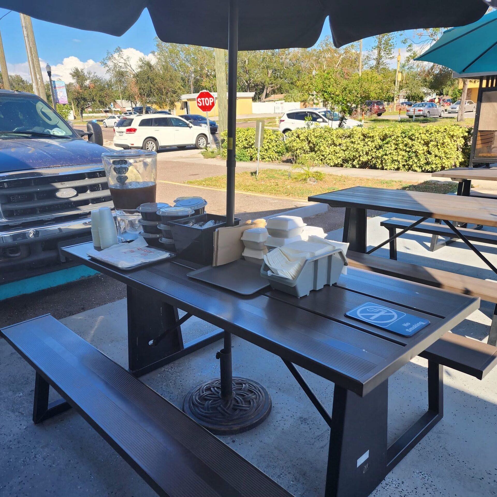 A picnic table on the 1Chick 1Bro patio, hedgerow and street behind