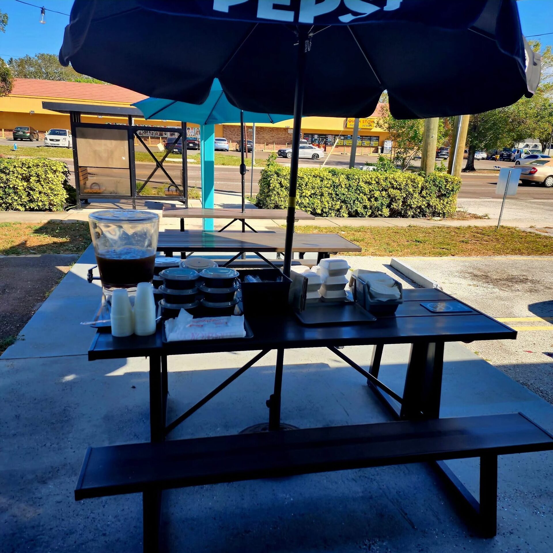 The 1Chick 1Bro patio: picnic table under an umbrella with a drink dispenser and to-go trays
