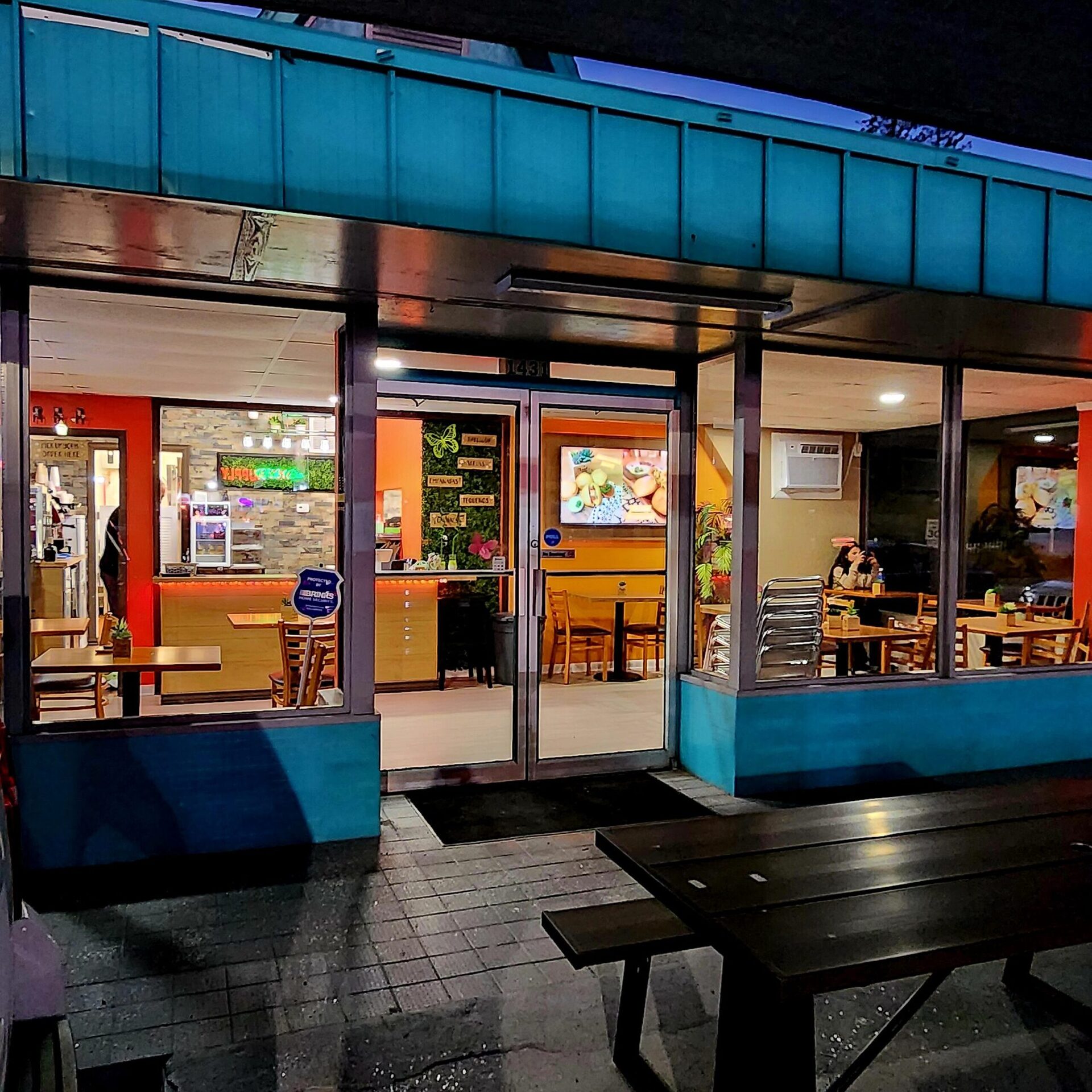 1Chick 1Bro Cafe Bistro at dusk on 49th St S in Gulfport — lit windows, teal storefront and picnic tables out front
