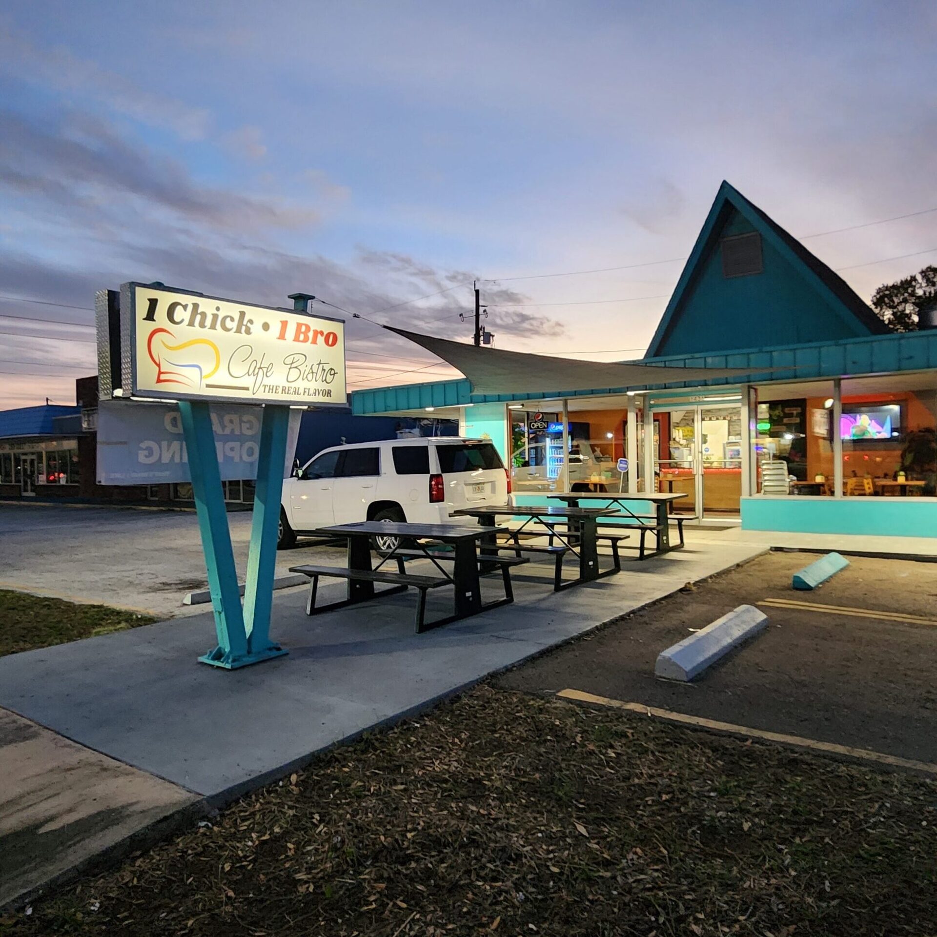 The 1Chick 1Bro building and pylon sign at sunset on 49th St S, Gulfport, with patio tables lit